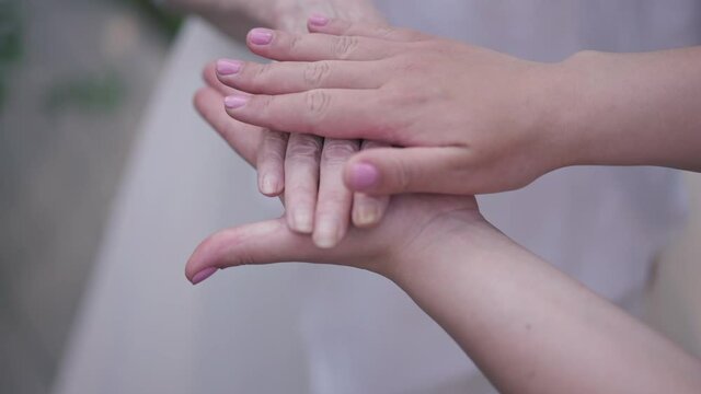 Close-up young and senior Caucasian women stacking hands in slow motion outdoors. Unrecognizable grandmother and granddaughter enjoying weekend leisure on spring summer day. Family concept