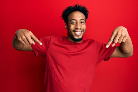 Young african american man with beard wearing casual red t shirt looking confident with smile on face, pointing oneself with fingers proud and happy.