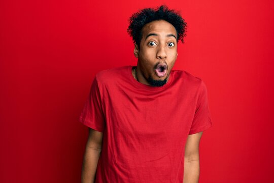 Young african american man with beard wearing casual red t shirt afraid and shocked with surprise expression, fear and excited face.