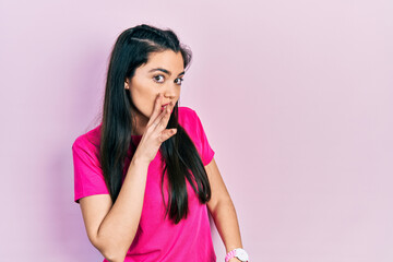 Young hispanic girl wearing casual pink t shirt hand on mouth telling secret rumor, whispering malicious talk conversation