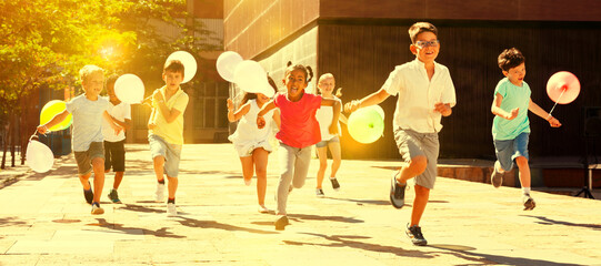 Smiling kids with balloons running in race and laughing at street at sunny day