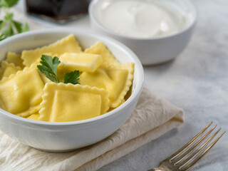 Ravioli with butter and a sprig of parsley. Sour cream sauce in the background. Nicely served table. Menu design, advertising, culinary blog, recipe book, home comfort.