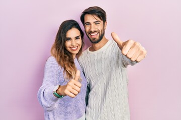 Young hispanic couple wearing casual clothes approving doing positive gesture with hand, thumbs up smiling and happy for success. winner gesture.