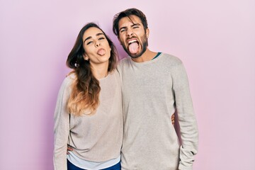 Young hispanic couple wearing casual clothes sticking tongue out happy with funny expression. emotion concept.