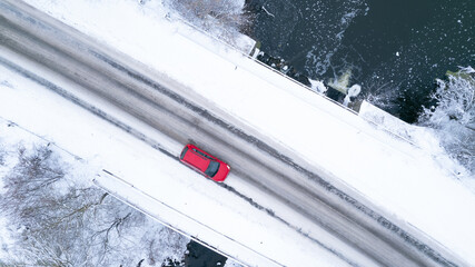 Aerial top down drone shot of Snowy landscape and winter road with red car on it. Forest road from above