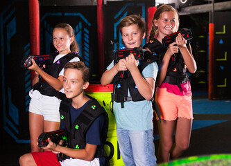 Group portrait of happy teenagers with laser guns having fun on dark lasertag arena..