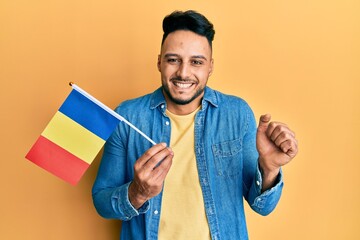 Young arab man holding romania flag screaming proud, celebrating victory and success very excited...
