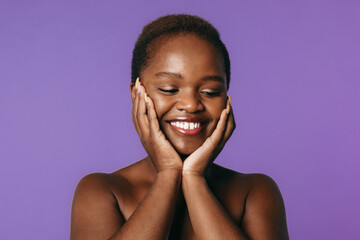 Portrait of an African black woman touching her face with both hands. posing over purple background. Beauty skin female face. Natural beauty.