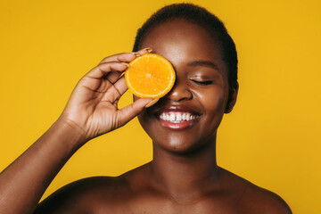 Portrait of an african girl covering eye with orange slice isolated over orange color background....