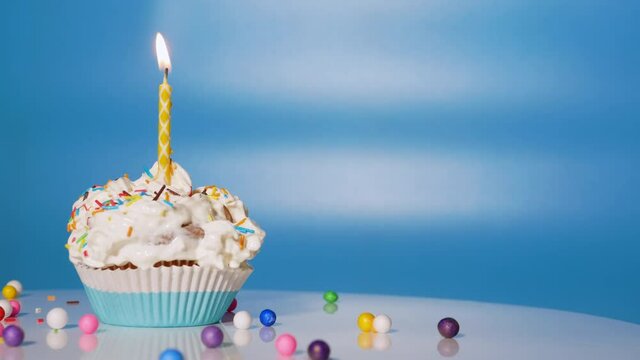 Festive cream cupcake on the turntable. Beautiful birthday greetings for a child, birthday cupcake with candles and decorations on a blue background. Copy space.