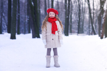 Full length portrait of cute beautiful pretty girl kid happy cheerful lovely child is smiling walking in snowy park at winter cold frosty day with snow looking at camera in warm clothes hat and gloves