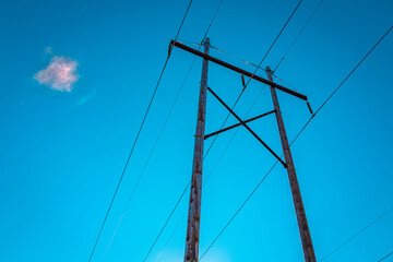 Electricity pole and power cables, and a piece of pink white cloud on turquoise-colored sky...