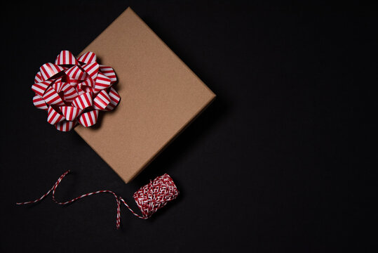cardboard gift box with a red and white bow with red and white braid on a black ibl background on top