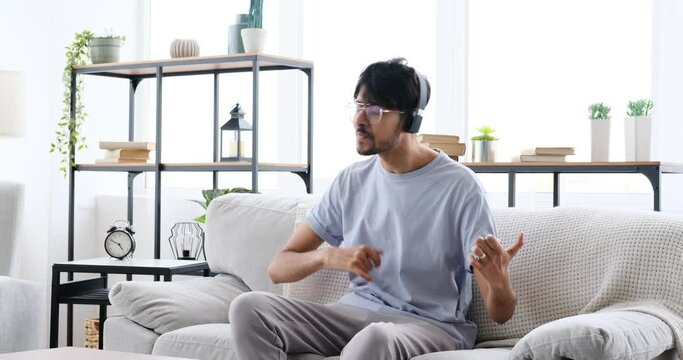 Crazy Man Having Fun Listening Music Using Headphones While Playing Air Guitar And Drum On Sofa In The Living Room