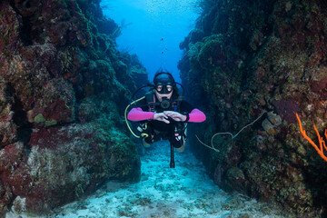 A young female scuba diver explores a canyon in a tropical Caribbean reef. Topographical features like this are relatively common in the Cayman Islands where this image was shot