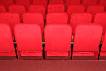 Fototapeta premium red armchairs. Empty concert hall, theater chairs background ... color photo, empty cinema or concert hall. The red chairs in the cinema hall are illuminated by a light beam. Selective focus