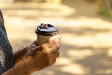 Closeup of woman hand holding disposable take away paper cup of hot coffee with copy space.