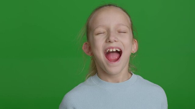 Cute school-age girl at an appointment with a doctor, a jaw surgeon or an orthodontist. Child opens his mouth wide and sticks out his tongue for inspection. close-up on green screen background