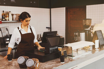 Beautiful young woman barista working in a coffee shop and restaurant standing in front of a counter using a smartphone to pay customers through modern, fast online applications : Selected Focus