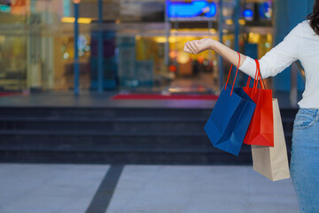 Asian woman holding shopping bags while standing in front of a shopping mall, shopping and selling concept. People. Payment.
