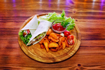 Chicken wrap sandwich with potatoes, vegetables and sauce on a wooden background.
