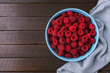 Red raspberry berry in plate on wooden table.
