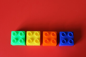 Buildable colored plastic blocks to play, build and organize on a red background as a concept of inclusion, diversity and plurality
