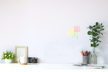 Creative workplace with photo frame, houseplant, coffee cup and pencil holder on white table. Copy space for your advertising text.