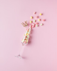 Crumbling pieces of marshmallow from a glass glass and a golden crown on a pink background. The concept of Valentine's Day.