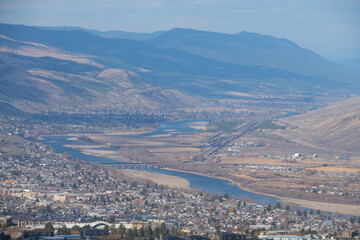 view of the mountains and river of the city of Kamloops in British Columbia Canada clue sky with clouds brown hills and urban development surrounding the Thompson River horizontal format room for type