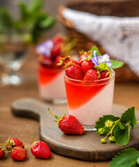 Creamy dessert with strawberry jelly in a glass with strawberry berry decor on a wooden background