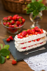 Pavlova dessert with strawberries and violet flowers as a decor on a wooden background