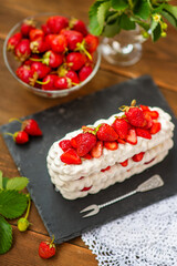 Pavlova dessert with strawberries and violet flowers as a decor on a wooden background