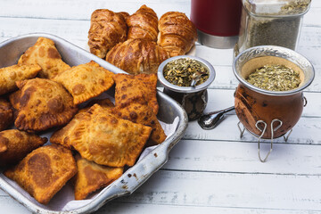 Mate, empanadas and croissants over a white wooden table. Family dinner