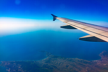 Fototapeta na wymiar View from the airplane window at a beautiful blue clear sky, earth, sea and the airplane wing