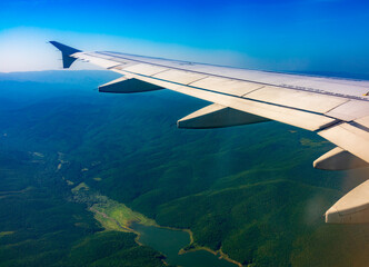 Fototapeta premium View of airplane wing, blue skies and green land during landing. Airplane window view.