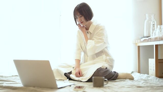 自宅の部屋でリラックスした雰囲気でノートPCを見る女性