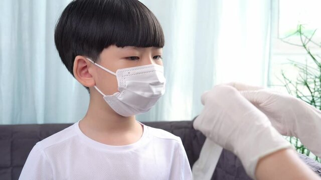 Mother pull medical take mask off, gently push swab stick into Asian child's nose to collect mucus sample with antigen test kit before go to school. Covid 19 new normal protection and safety.