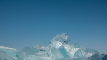 A bizarre block of turquoise ice hummocks against a clear blue sky. Sun glare on the edges....