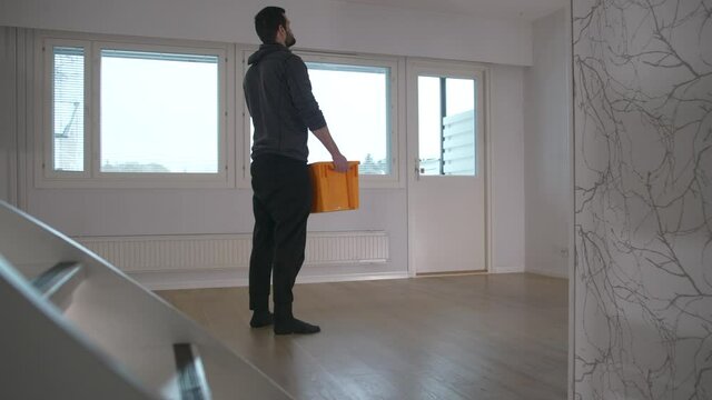 Young man picks up last box from empty room when moving out, static