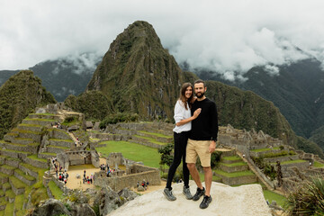 Happy couple poses in front of ruins of inca's citadel Machu Picchu in Peru