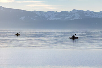Fototapeta premium Two kayakers paddling in winter on a hazy day at Lake Tahoe