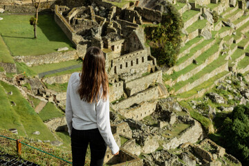 A young woman looks at the ruins of Machu Pichhu