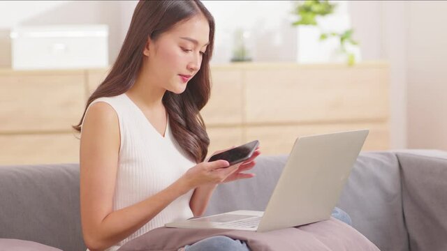 Beautiful Asian woman wear casual sweater working on laptop smile and talking with customer in smartphone to get idea requirement for success job at home.Freelance woman working online sale marketing