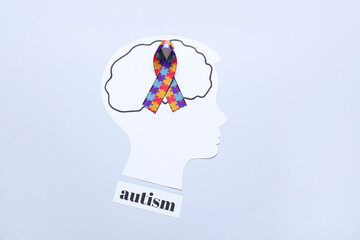 Paper human head with awareness ribbon and word AUTISM on light background