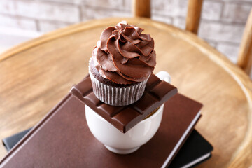 Tasty chocolate cupcake with cup and books on wooden chair