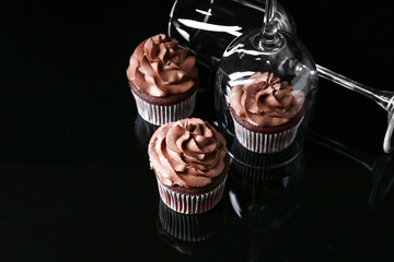 Tasty chocolate cupcakes with wine glasses on dark background