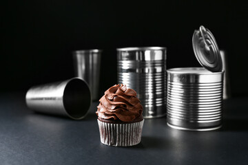 Tasty chocolate cupcake with tin cans on dark background