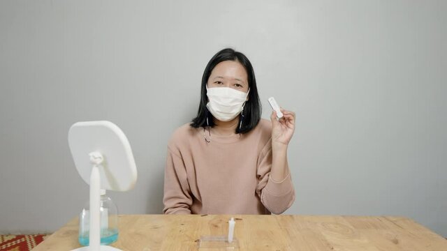 4K, A long-haired Asian woman used a rapid antigen test kit to self-test the COVID-19 epidemic at home and has shown a negative result of no COVID-19, showing 1 red line. show a happy expression.