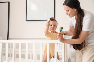 Young mother giving toys to her little baby in crib at home